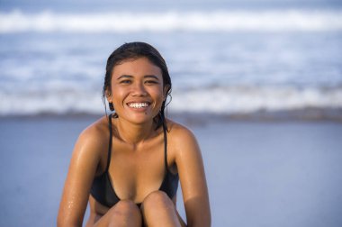 Genç, egzotik ve çekici bikinili gülümseyen, rahat ve kaygısız bir Asyalı kız tropik sahilde mutlu ve neşeli tatiller geçiriyor ve denizde eğleniyor.