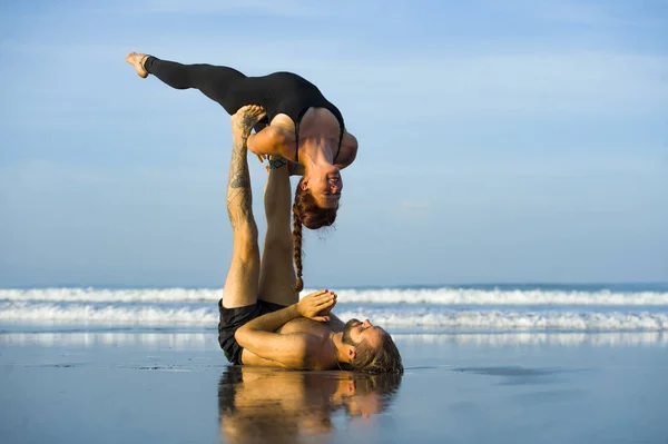 Young attractive and beautiful acrobat couple practicing acroyoga exercise concentrated keeping balance practiing yoga on the beach in relaxation and meditation concept — Stock Photo, Image