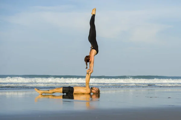 Young attractive and beautiful acrobat couple practicing acroyoga exercise concentrated keeping balance practiing yoga on the beach in relaxation and meditation concept — Stock Photo, Image