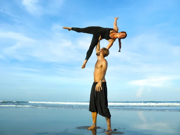 Young attractive and beautiful acrobat couple practicing acroyoga exercise concentrated keeping balance practicing yoga on the beach in relaxation and meditation concept — Stock Photo, Image