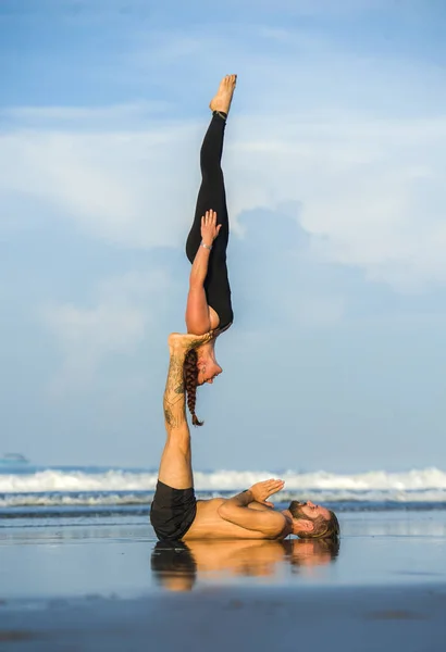 Young attractive and beautiful acrobat couple practicing acroyoga exercise concentrated keeping balance practiing yoga on the beach in relaxation and meditation concept — Stock Photo, Image