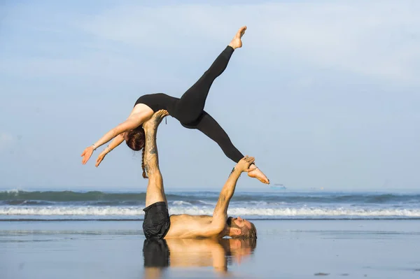 Young attractive and beautiful acrobat couple practicing acroyoga exercise concentrated keeping balance practiing yoga on the beach in relaxation and meditation concept — Stock Photo, Image