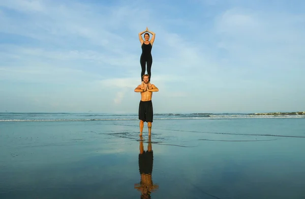 Young attractive and beautiful acrobat couple practicing acroyoga exercise concentrated keeping balance practiing yoga on the beach in relaxation and meditation concept — Stock Photo, Image