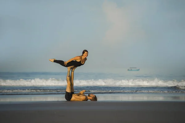 Young attractive and beautiful acrobat couple practicing acroyoga exercise concentrated keeping balance practiing yoga on the beach in relaxation and meditation concept — Stock Photo, Image
