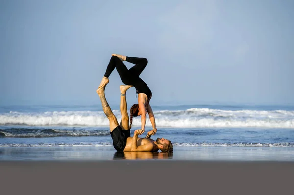 Молода приваблива і красива пара акробатів, що практикують вправи акройога, зосереджена на збереженні балансу практикуючих йоги на пляжі в концепції релаксації та медитації — стокове фото