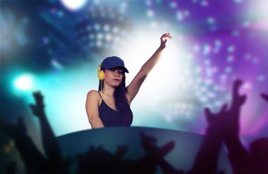 Genç, çekici ve mutlu Asyalı bir Japon DJ kadın gece kulübünde DJ ekipmanı ve kulaklık kullanarak tekno müziği remiksliyor. Gece kulüplerinde eğlenirken arka planda ışıklar var.