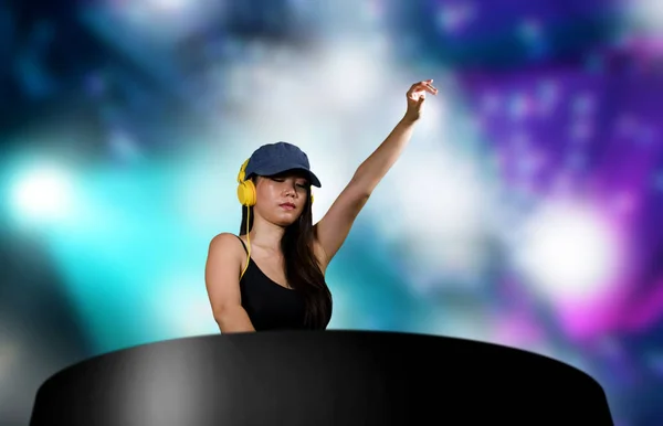 Jong aantrekkelijk en gelukkig aziatisch japans dj vrouw remixen techno muziek met behulp van dj gear en hoofdtelefoon in nachtclub met lichten achtergrond in clubbing plezier 's nachts — Stockfoto