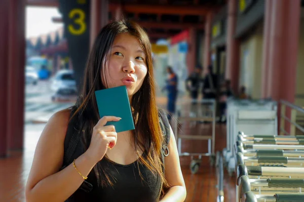 young happy and attractive Asian Chinese backpacker woman smiling excited at airport arrival or departure holding passport in holidays tourist trip and student travel fun