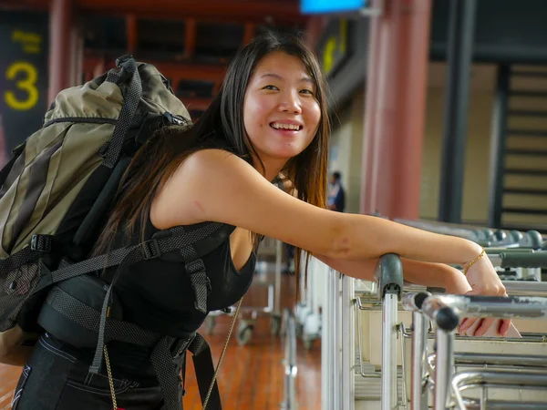 Genç, mutlu ve çekici Asyalı sırt çantalı kadın havalimanı gelişinde ya da gidişinde heyecanla gülümsüyor. Tatil gezisi ve öğrenci seyahatinde büyük bir sırt çantası taşıyor.