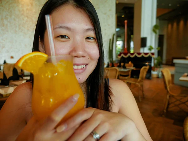 Joven feliz y relajado asiático chino turista mujer beber sano orance jugo en hotel café o restaurante resort sonriendo alegre en turismo viaje y estilo de vida —  Fotos de Stock
