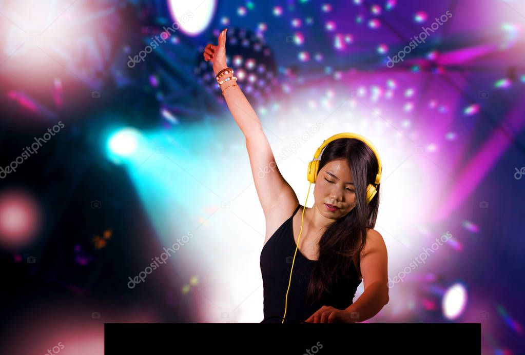 young beautiful and attractive Asian Korean DJ woman remixing music at night club wearing headphones isolated on flashes and laser lights background in clubbing party concept