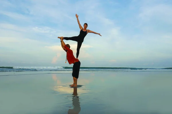 healthy and attractive fit couple of acrobats  doing acroyoga balance and meditation exercise on beautiful desert beach practicing balance and harmony posing