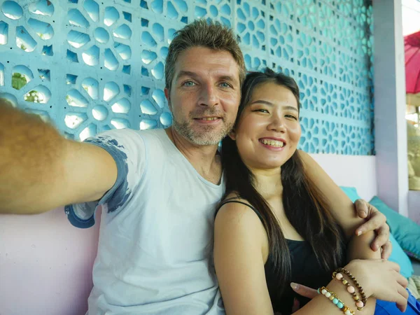 happy mixed ethnicity couple in love smiling cheerful with handsome Caucasian man and beautiful Asian Chinese woman taking selfie photo together with mobile phone