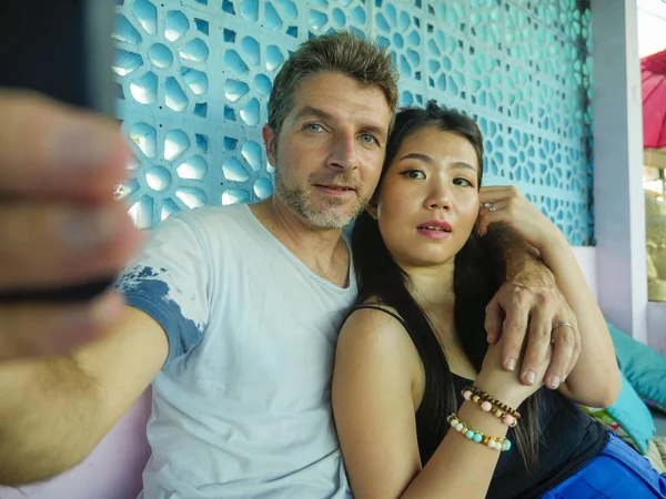 Счастливая смешанная этническая пара влюбленная улыбается веселый с красивым кавказским мужчиной и красивая азиатская японская женщина делает селфи фото вместе с мобильным телефоном — стоковое фото