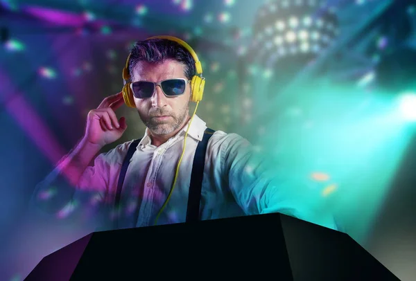 Young attractive and cool DJ in shirt and suspenders remixing music at night club using headphones in party strobo and flash lights background in clubbing and nightlife concept — Stock Photo, Image
