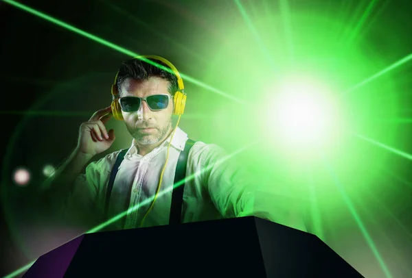 Young attractive and cool DJ in shirt and suspenders remixing music at night club using headphones in party strobo and laser lights background in clubbing and nightlife — Stock Photo, Image