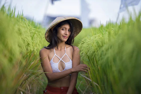 Young happy and beautiful latin woman playing with traditional Asian farmer hat smiling having fun posing sexy isolated on green rice field in Asia tourist trip — Stock Photo, Image