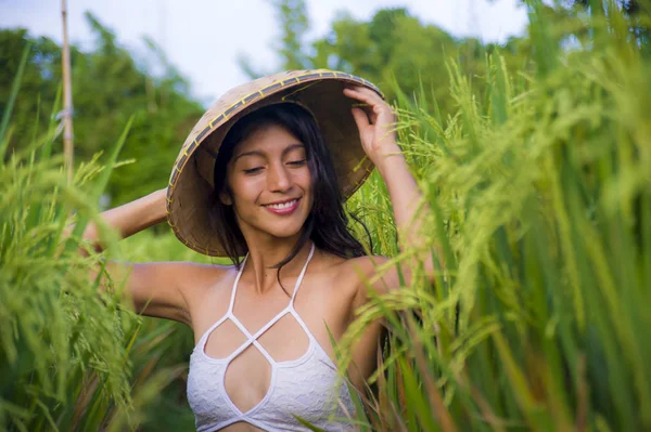 Giovane donna latina felice e bella che gioca con tradizionale cappello contadino asiatico sorridente divertendosi posa sexy isolato sul campo di riso verde in Asia viaggio turistico — Foto Stock