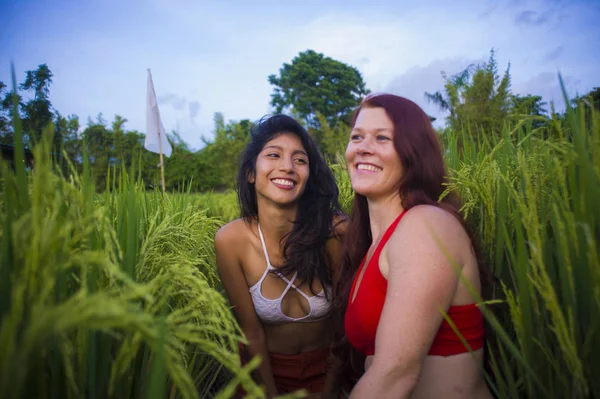 young beautiful latin woman and her attractive red hair girlfriend both girls enjoying Summer holidays together walking on rice field smiling happy relaxed in diversity ethnicity