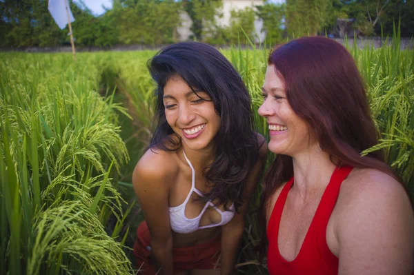 Jovem bela menina latina e sua atraente namorada de cabelo vermelho ambas as mulheres desfrutando de férias de verão juntos andando no campo de arroz sorrindo feliz relaxado na diversidade étnica — Fotografia de Stock