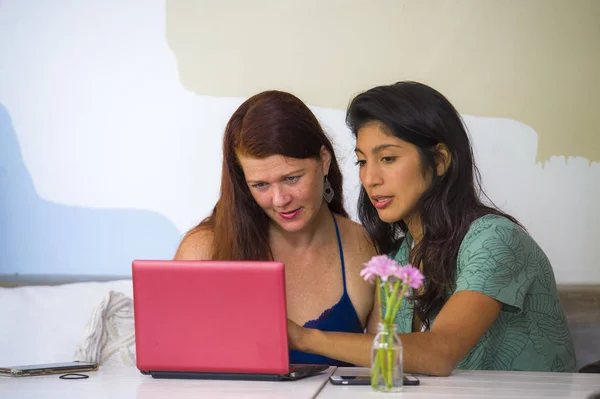 Joven mujer caucásica feliz y hermosa chica hispana que trabaja en la cafetería de la oficina con el ordenador portátil discutir como socios de negocios digitales y amigos étnicos diversidad — Foto de Stock