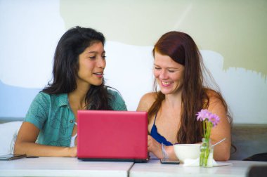 Genç, mutlu, beyaz ve Latin kadınlar ofis kafesinde dizüstü bilgisayarla dijital iş ortağı ve etnik çeşitlilik arkadaşı olarak tartışıyorlar.