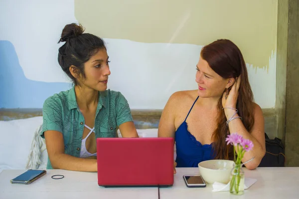 Jóvenes felices y hermosas mujeres caucásicas y latinas que trabajan en la cafetería de la oficina con computadora portátil discutiendo como socios de negocios digitales y amigos étnicos diversidad — Foto de Stock