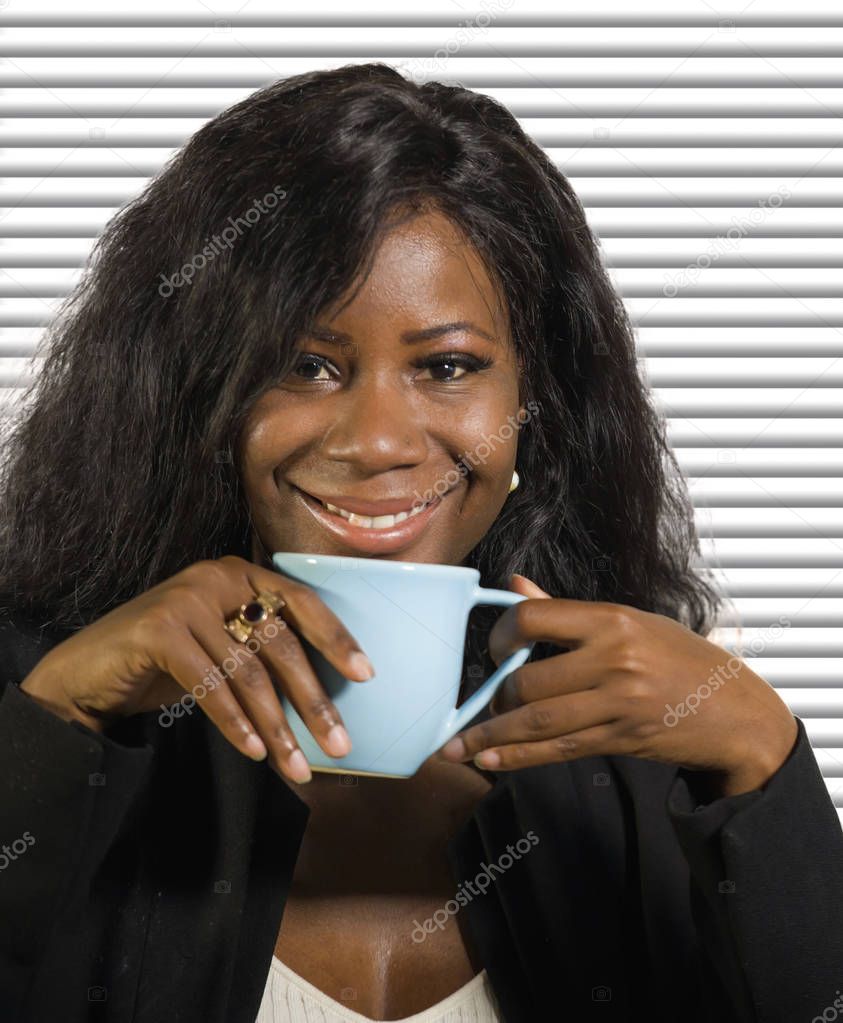 young beautiful and successful black afro American businesswoman drinking coffee smiling confident and relaxed on office blinds background in woman success