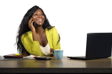 Genç, mutlu ve çekici, Afro-Amerikan iş kadını kahve içiyor. Ofis masasında rahatça çalışıyor ve cep telefonuyla konuşuyor.