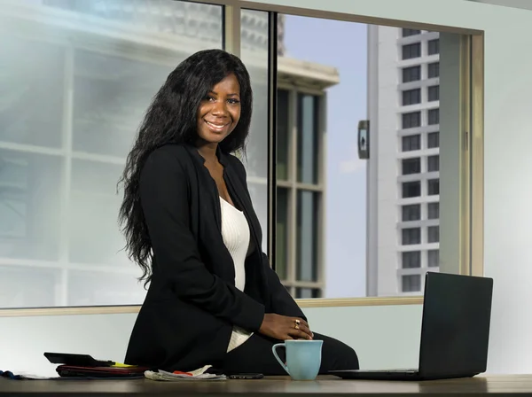 Joven hermosa y feliz mujer de negocios afroamericana posando corporativo trabajando en escritorio moderno de la computadora de la oficina en frente de la ventana sonriendo con éxito y confiado —  Fotos de Stock