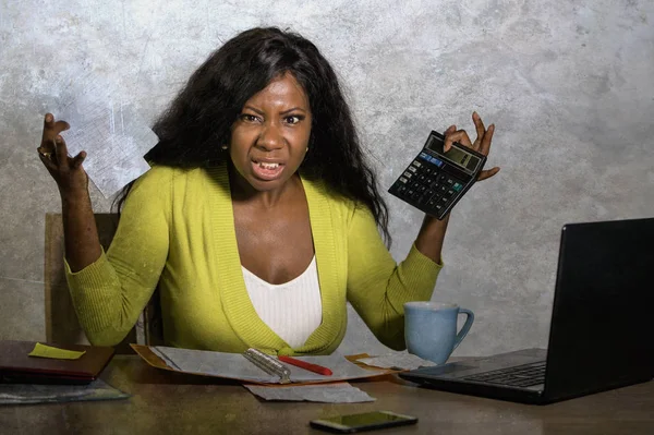 Jong gestresst en overweldigd zwart afro Amerikaanse vrouw doen binnenlandse boekhouding met calculator gevoel boos en vasthouden van papierwerk in financiële stress — Stockfoto