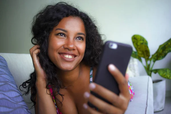 Jovem bonita e feliz mista etnia caucasiana e negra afro-americana deitada em casa sofá usando o aplicativo do telefone móvel namoro on-line sorrindo alegre — Fotografia de Stock