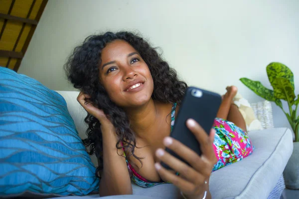 若いです美しく、幸せな混合民族白人と黒人アフリカ系アメリカ人女性は携帯電話アプリを使用してホームソファに横たわっています日付オンライン笑顔陽気な — ストック写真