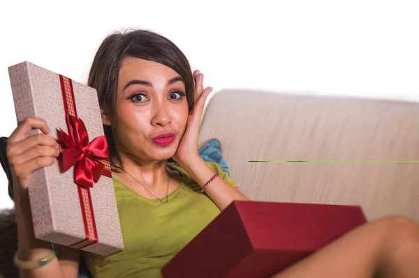 生活方式家庭肖像年轻美丽和快乐的亚洲印尼妇女举行生日或圣诞礼物打开礼品盒欢快和兴奋地坐在客厅沙发上 — 图库照片