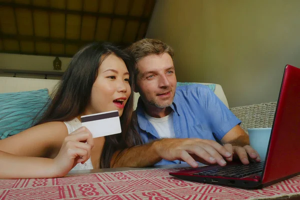 Молодая счастливая и красивая смешанная этническая пара с мужем или парнем кавказца и азиатская китаянка жена или подружка делают покупки онлайн вместе дома — стоковое фото