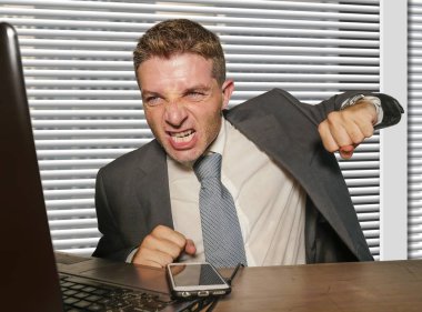 Genç, stresli ve takım elbiseli bir iş adamı dizüstü bilgisayarı yumrukluyor sinirli ve sinirli bir şekilde ofis masasında çalışıyor. Stres sorunu yaşıyor.