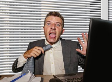 Genç, stresli ve takım elbiseli bir iş adamı kravatını çekiyor. Ofis bilgisayarında çalışırken çaresizce bağırıyor.