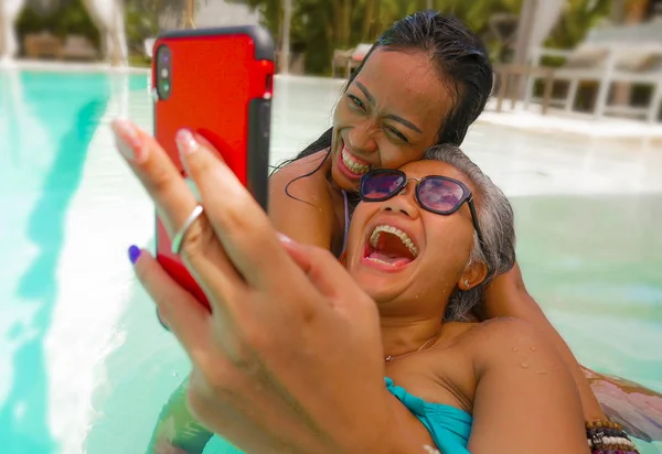 열대 해변 리조트 수영장에서 여름 휴가를 즐기는 아시아 여자 친구의 라이프 스타일 야외 초상화 휴대 전화 재생과 셀카 사진을 찍고 — 스톡 사진