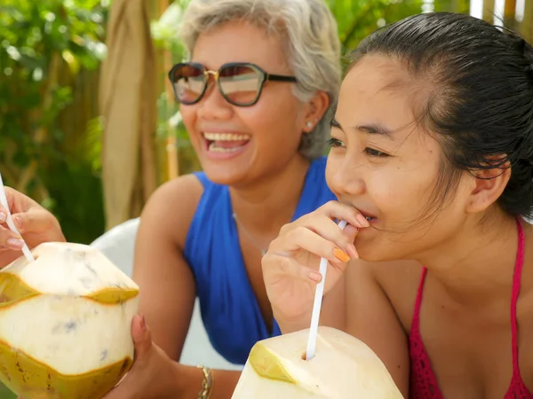 Портрет счастливой и красивой азиатской индонезийской девочки-подростка, наслаждающейся летними каникулами, пьющей кокос в тропическом саду курорта вместе со своей матерью — стоковое фото