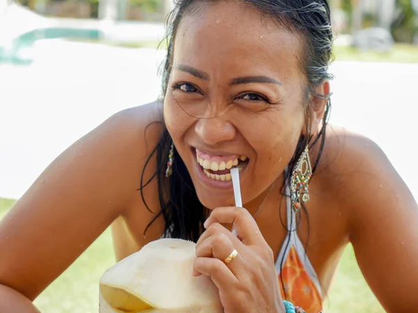 Estilo de vida retrato natural de 30 ou 40 anos mulher asiática indonésia feliz e atraente em biquíni beber água de coco na piscina resort tropical sorridente alegre — Fotografia de Stock