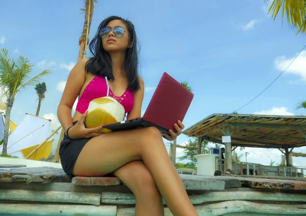 Jovem bonita e feliz asiática indonésia adolescente em biquíni no resort tropical piscina networking relaxado e resfriado com computador portátil sorrindo — Fotografia de Stock