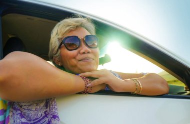 çekici ve mutlu orta yaşlı Asya Endonezyalı kadın 40s veya 50s gri saçlı ve güzel bir gülümseme penceresinden rahat bakarak gün batımı zevk arabasında oturan