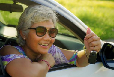 çekici ve mutlu orta yaşlı Asya Endonezyalı kadın 40s veya 50s gri saçlı ve güzel bir gülümseme pencere rahat ve neşeli anahtarı tutan onu yeni arabada oturan