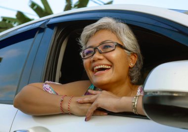 çekici ve mutlu orta yaşlı Asya Endonezyalı kadın 40s veya 50s gri saçlı ve güzel bir gülümseme arabada oturan doğanın keyfini pencereden rahat bakarak