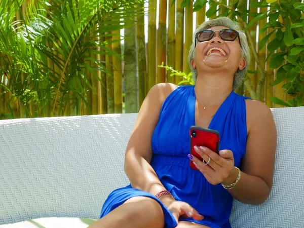 Feliz e atraente asiático indonésio mulher relaxado no tropical praia resort jardim rede alegre no celular sorrindo desfrutar de férias — Fotografia de Stock