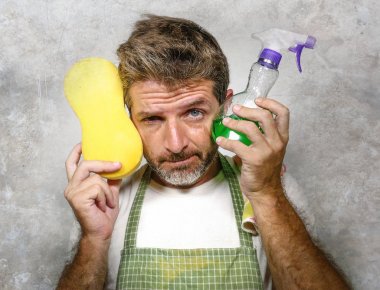 apron tutan adam sünger ve deterjan sprey duygu boğulmuş ve tembel ve rahatsız yüz temizlik ve yıkama ev ev işleri yapıyor sıkılmış