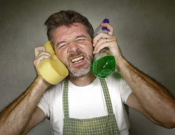 Człowiek w fartuch trzymając gąbki i detergentu spray uczucie przytłoczeni i znudzony robiąc domowe sprzątanie i mycie krzyczeć zdesperowany w stres — Zdjęcie stockowe