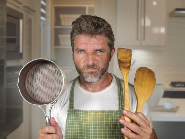 ev işleri ve pişirme görevi ev mutfağında üzgün ve tembel duygu apron tutan kaşık ve tava çekici mutsuz ve ezilmiş ev aşçı adam