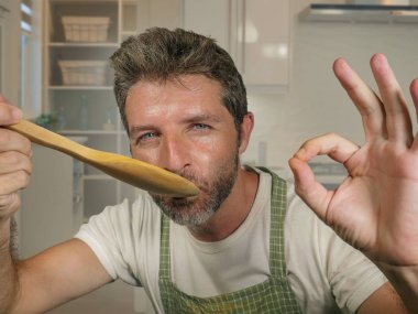 modern mutfakta ev işi ve pişirme hobi zevk kaşık ile apron gülümseyen neşeli ve büyüleyici tatma güveç mutlu ve çekici ev aşçı adam