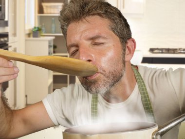 modern mutfakta ev işi ve pişirme hobi zevk kaşık ile apron gülümseyen neşeli ve büyüleyici tatma güveç mutlu ve çekici ev aşçı adam